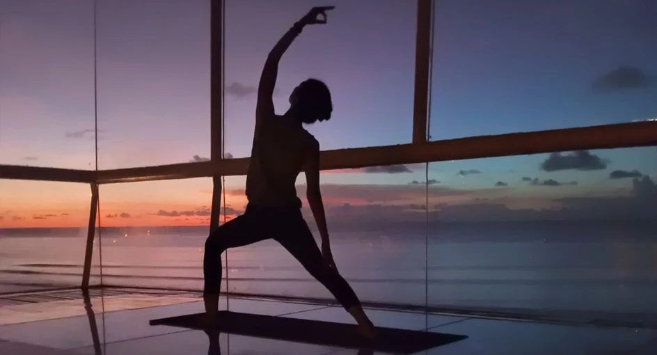 A yoga pose silhouetted against the sunset through floor-to-ceiling glass